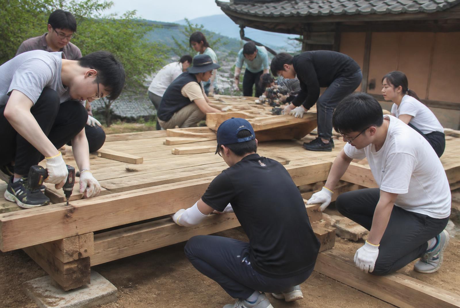 Student volunteers assembling a wooden pyeongsang platform by hand in the village