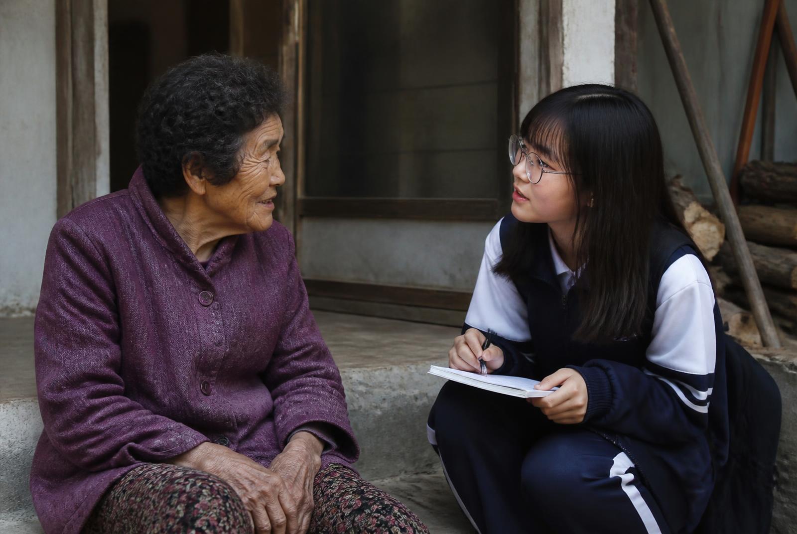 A student volunteer interviewing an elderly resident outside her home in Gwanjeong 3-ri